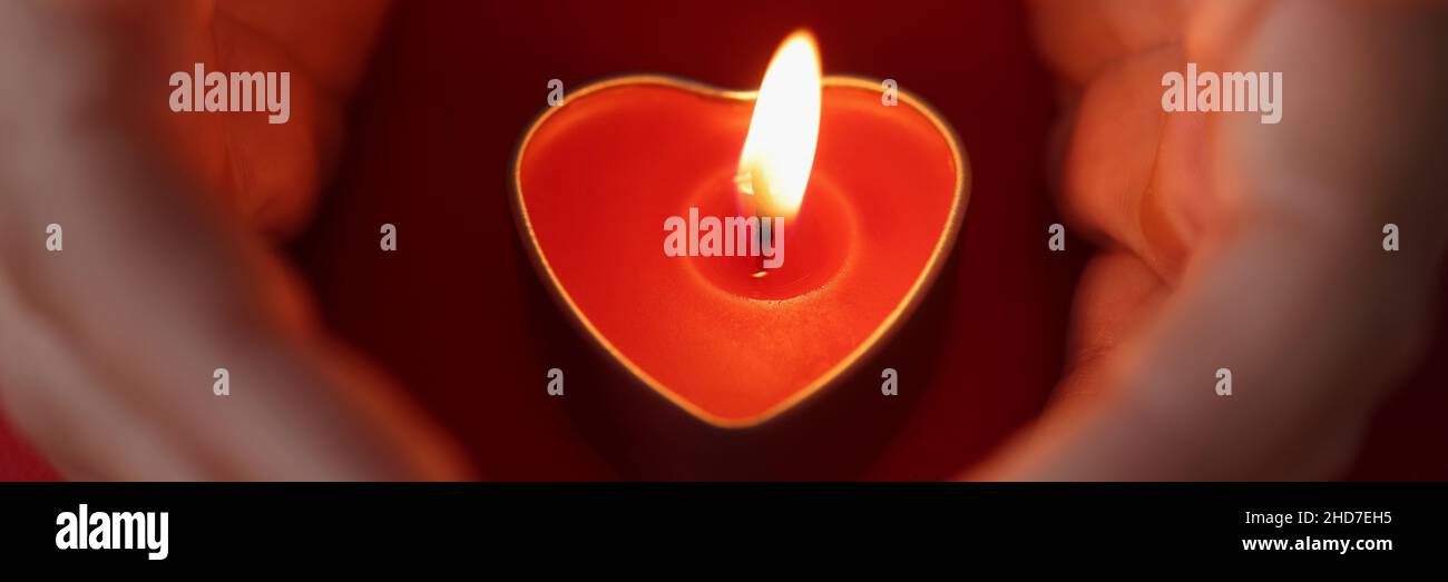 Les mains des femmes protègent soigneusement les bougies sous forme de coeur avec feu brûlant Banque D'Images