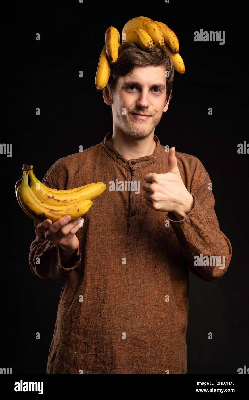 Jeune beau grand homme blanc mince avec des bananes de cheveux bruns sur la  tête pouces avec chemise marron sur fond noir Photo Stock - Alamy