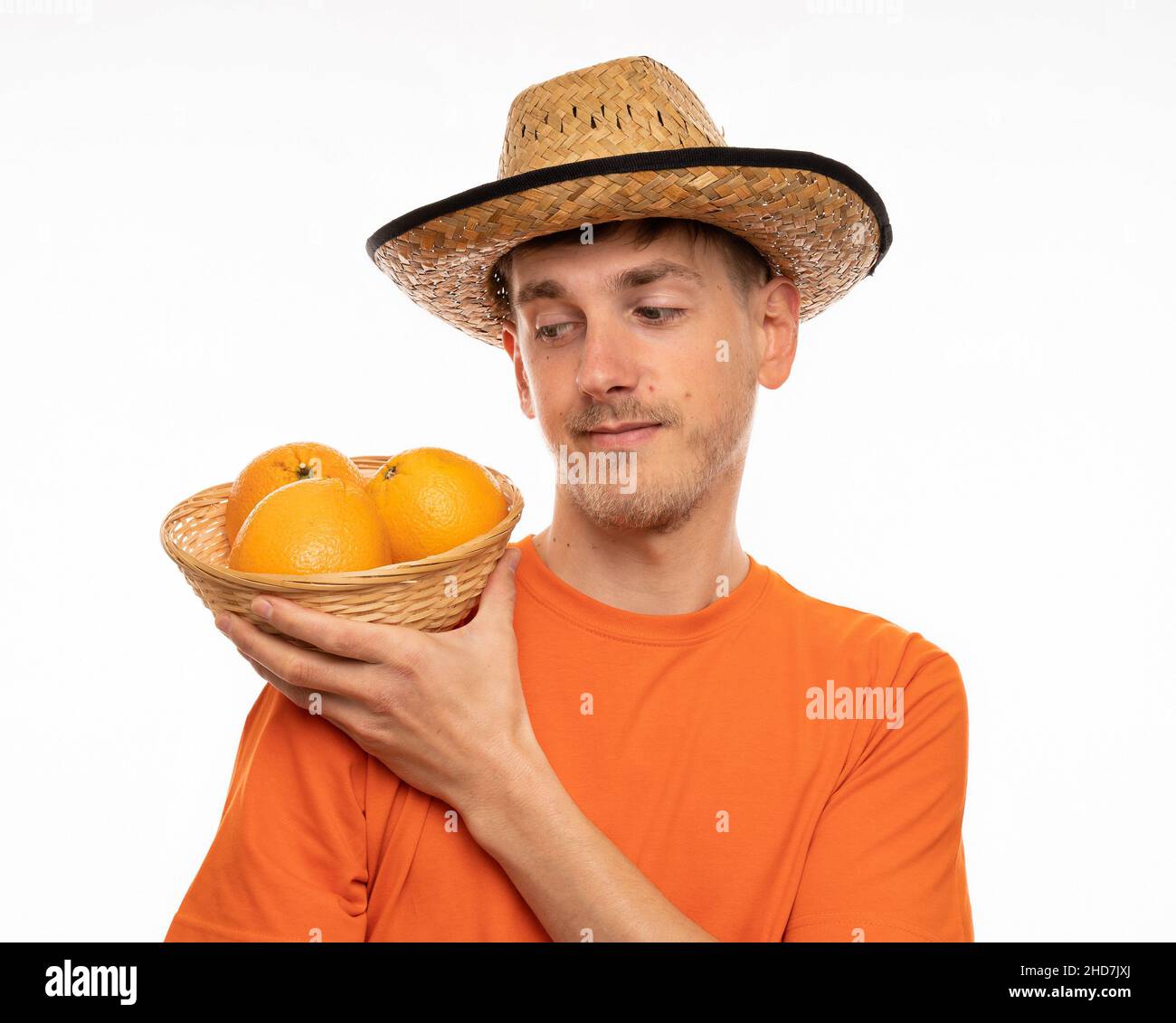 Jeune beau grand homme blanc mince avec des cheveux bruns oranges sur l'épaule dans une chemise orange avec chapeau de paille isolé sur fond blanc Banque D'Images