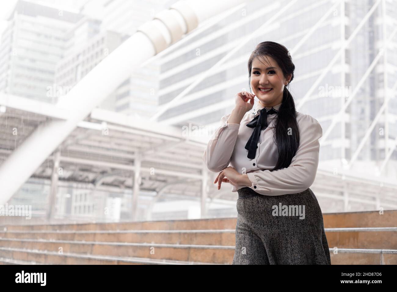 Portrait sourire asiatique ouvrier de bureau fille avec les bras croisés à l'extérieur et l'espace de copie.Souriante femme d'affaires thaïlandaise heureuse avec fond de ville. Banque D'Images