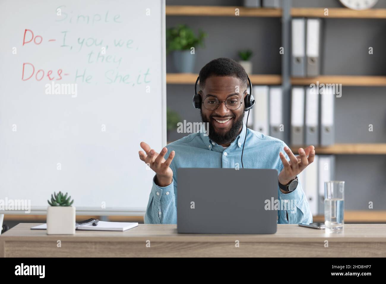 Joyeux jeune africain américain tuteur ou des gestes d'enseignant avec les mains et regarde l'écran de pc dans la maison Banque D'Images