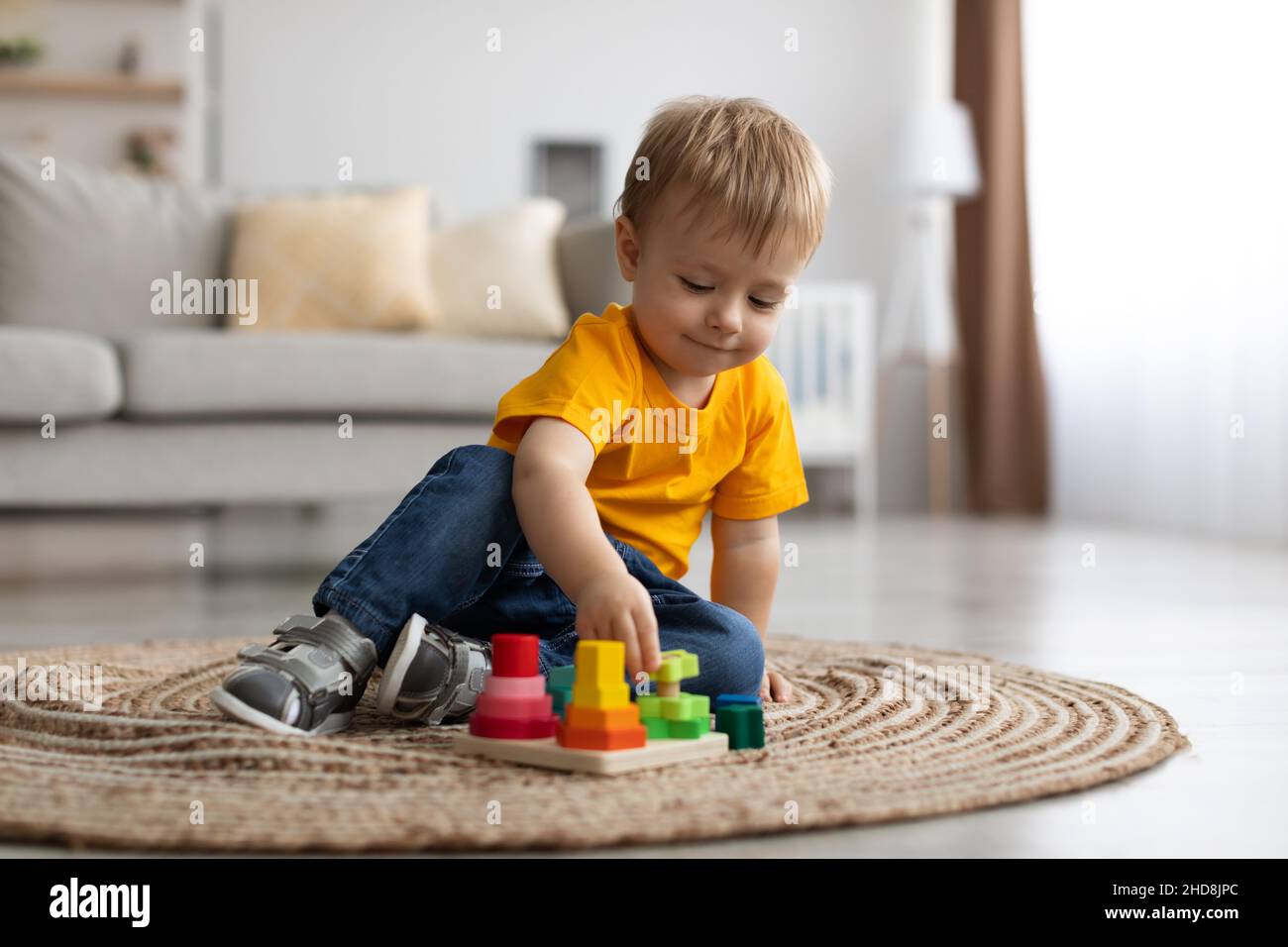 Adorable petit garçon jouant avec un jouet éducatif en bois à la maison, assis sur la moquette dans le salon, espace de copie Banque D'Images