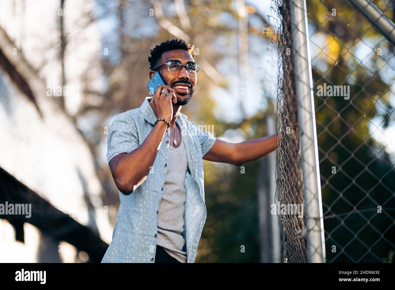 Beau afro homme en utilisant son smartphone dans la rue en souriant s'appuyant sur une clôture Banque D'Images