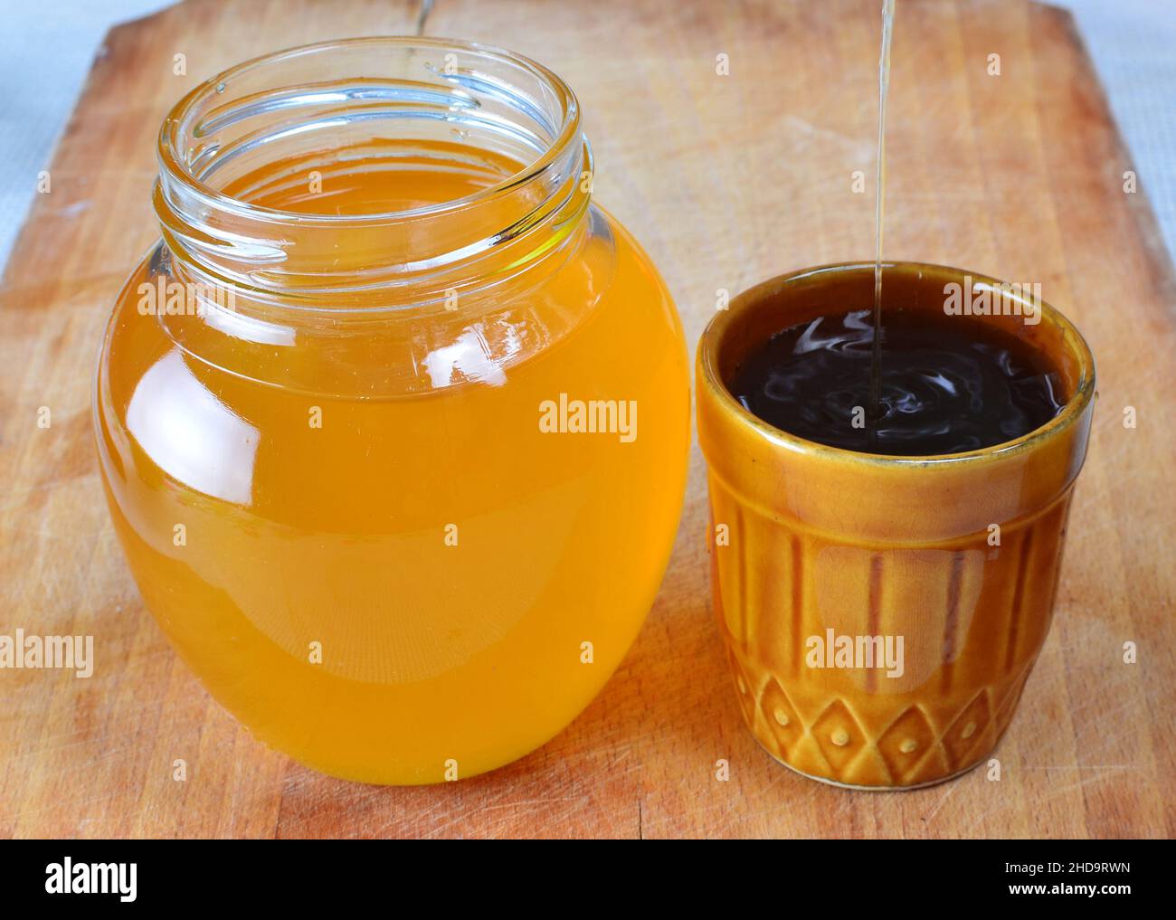 Du miel frais naturel biologique est versé dans une petite tasse rustique à côté d'un pot rempli de miel. Banque D'Images