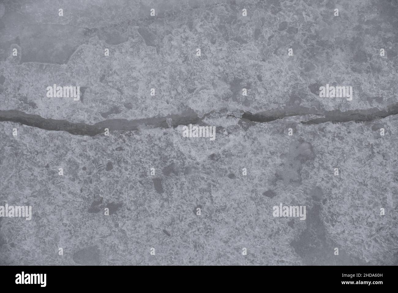 Une grande fissure traverse le cadre à travers la texture complexe de glace naturellement formée sur la surface d'une rivière gelée. Banque D'Images