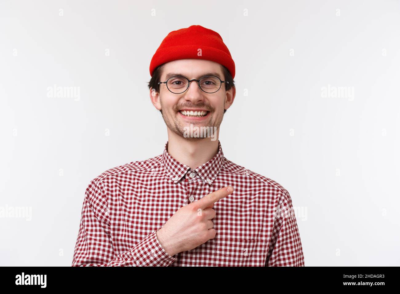 Gros plan portrait beau sympathique-look hipster mâle dans le bonnet et les verres rouges, souriant satisfait et heureux, pointage doigt coin supérieur droit Banque D'Images