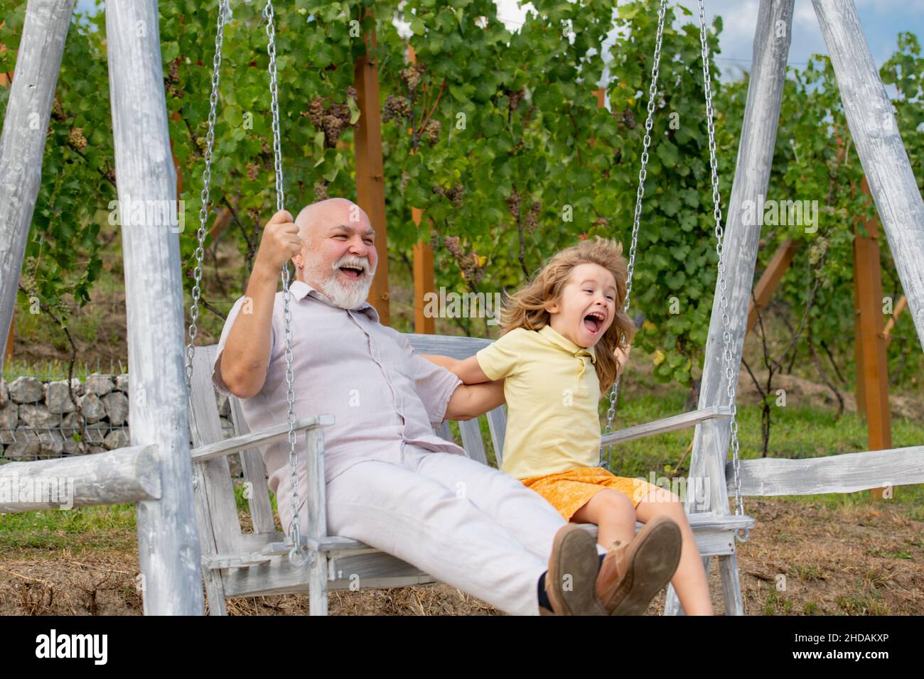 Jeune petit-fils et grand-père balançant dans le jardin de printemps.Grand-père et petit-fils assis sur le balançoire dans le parc. Banque D'Images