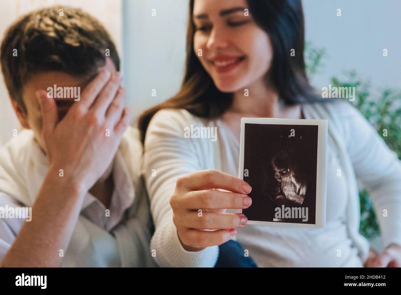 Jeune femme enceinte heureuse tenant une échographie de grossesse, montrant l'image de l'échogramme à un mari agréablement surpris pleurant du bonheur.Couple familial Banque D'Images