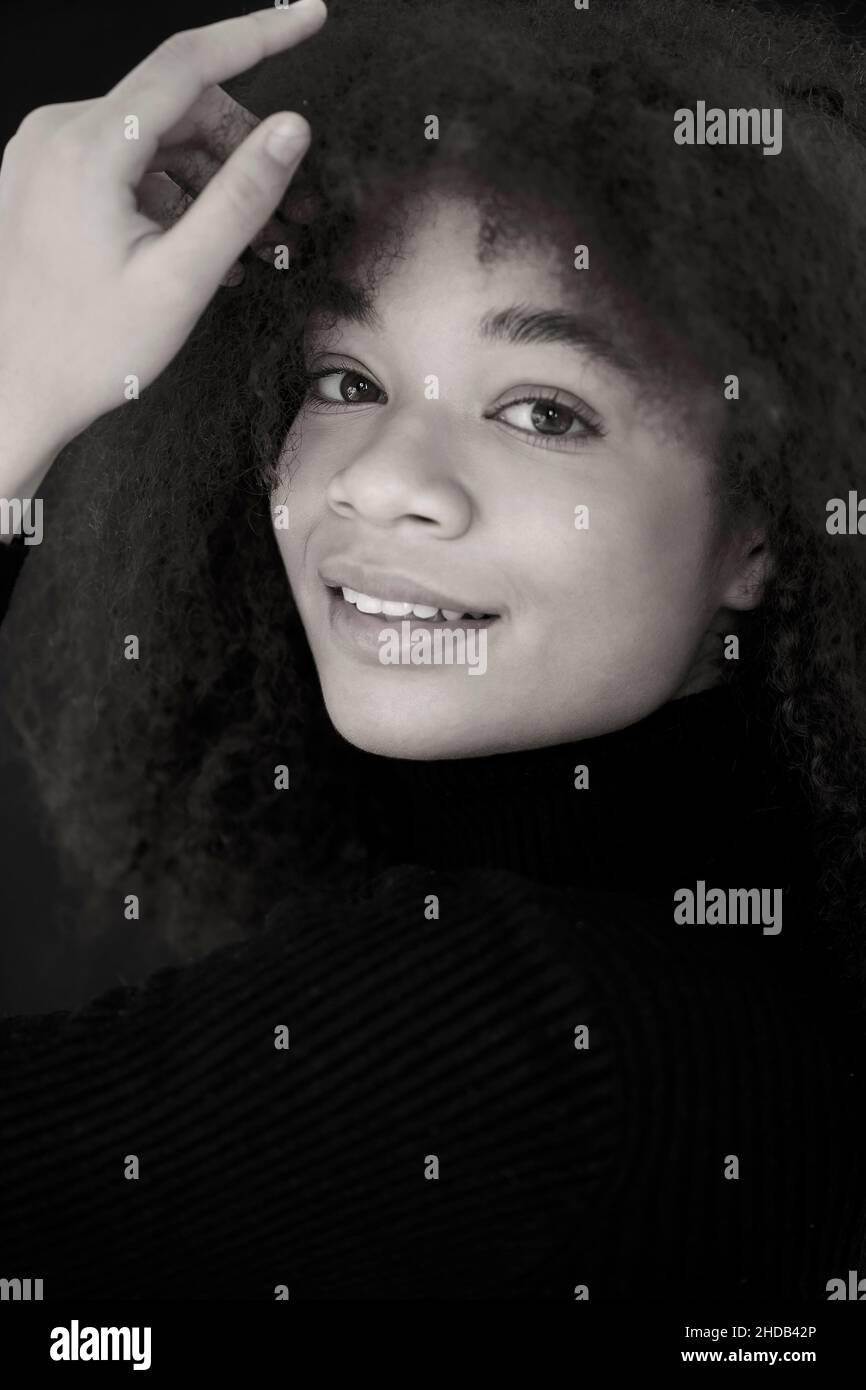 Portrait d'une femme afro-américaine élégante et souriante vêtue de vêtements noirs regardant l'appareil photo, posant isolée sur un arrière-plan sombre du studio.Jeune natur Banque D'Images