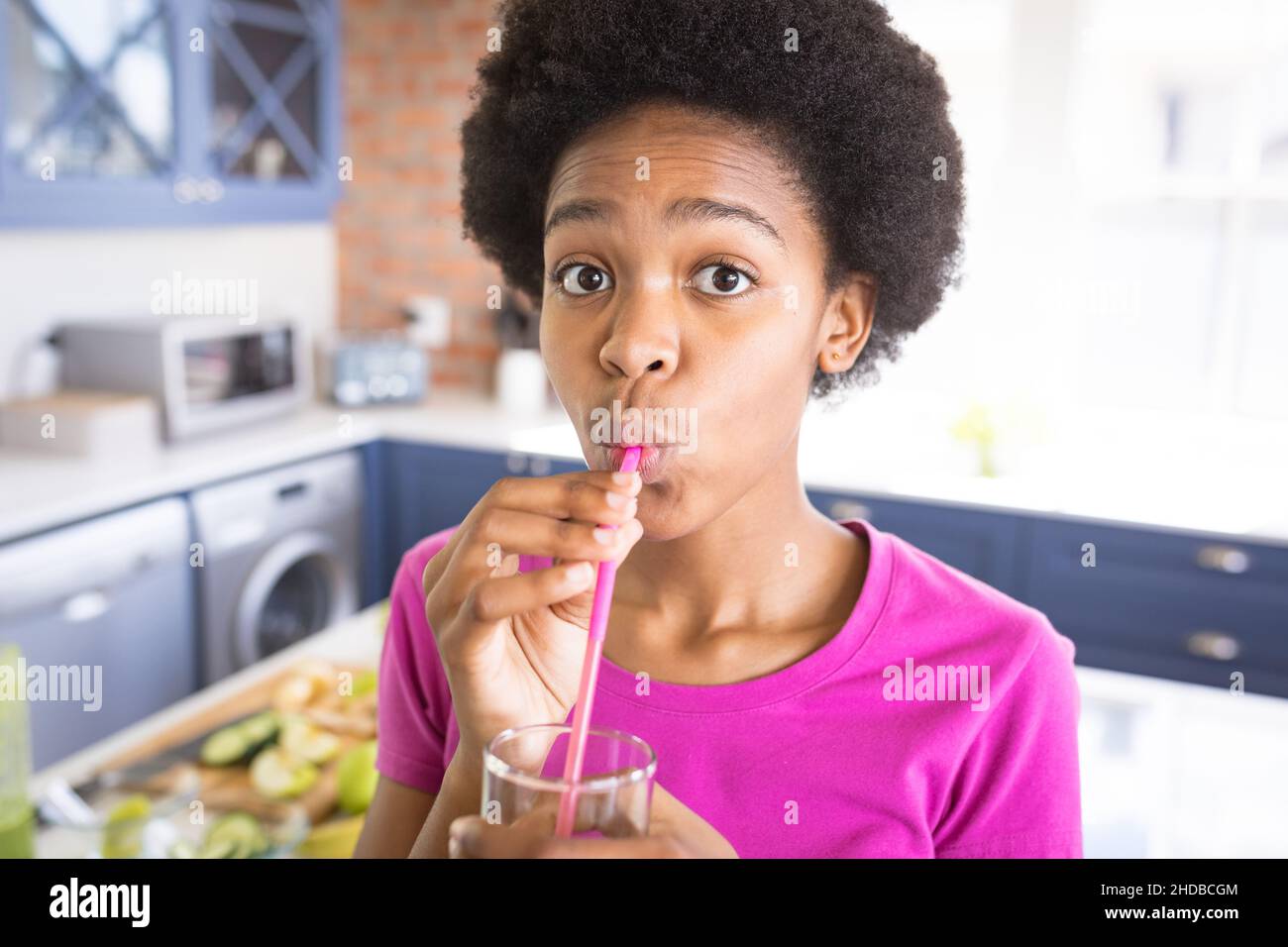 Portrait d'une fille afro-américaine qui boit du jus sain à la paille à la maison Banque D'Images