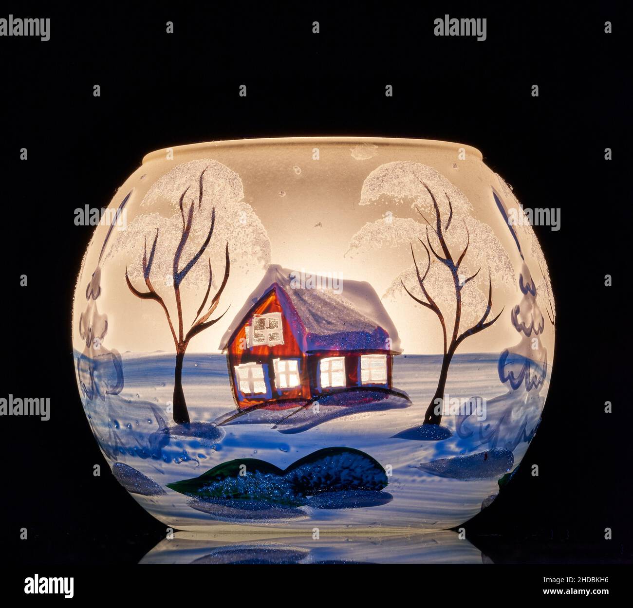Une tasse en verre peinte à la main avec un décor hivernal éclairé par une bougie à l'intérieur de la tasse.Un gros plan photographique utilisant la peinture légère. Banque D'Images