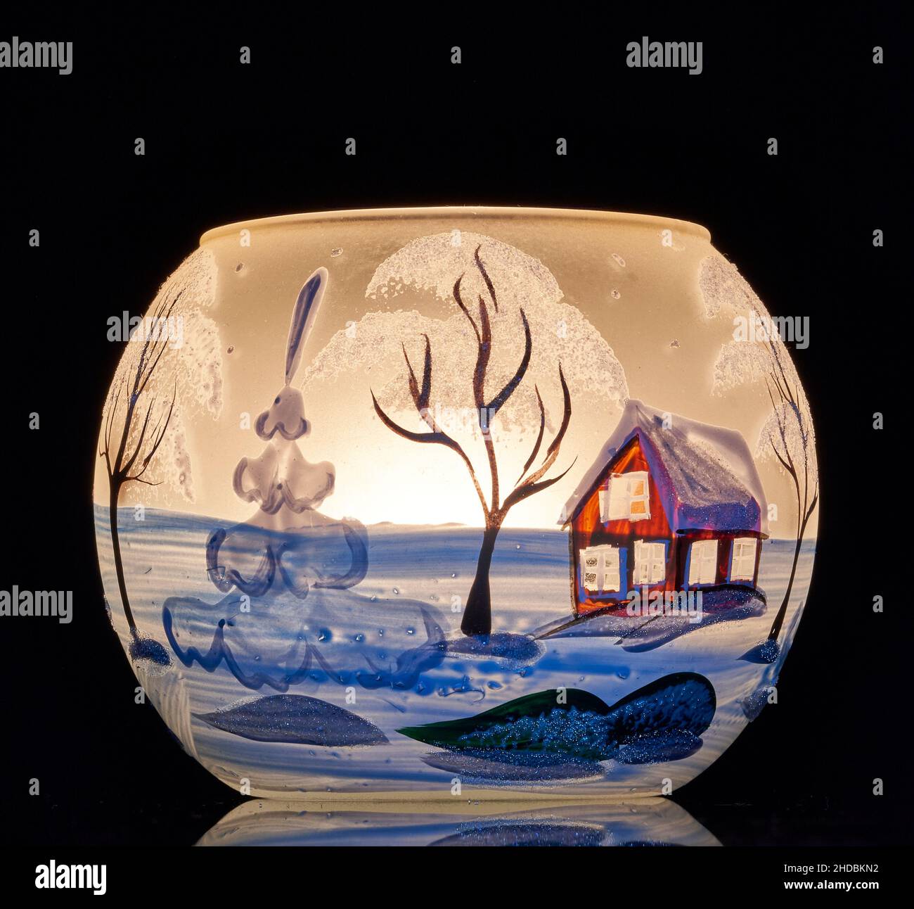 Une tasse en verre peinte à la main avec un décor hivernal éclairé par une bougie à l'intérieur de la tasse.Un gros plan photographique utilisant la peinture légère. Banque D'Images