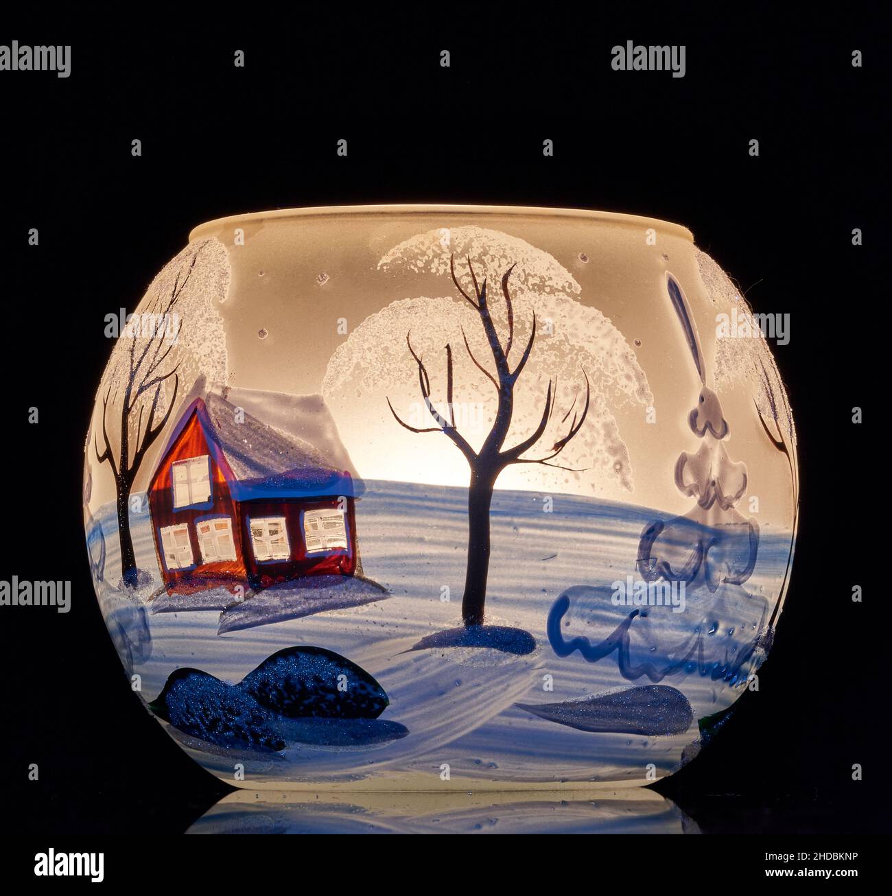 Une tasse en verre peinte à la main avec un décor hivernal éclairé par une bougie à l'intérieur de la tasse.Un gros plan photographique utilisant la peinture légère. Banque D'Images