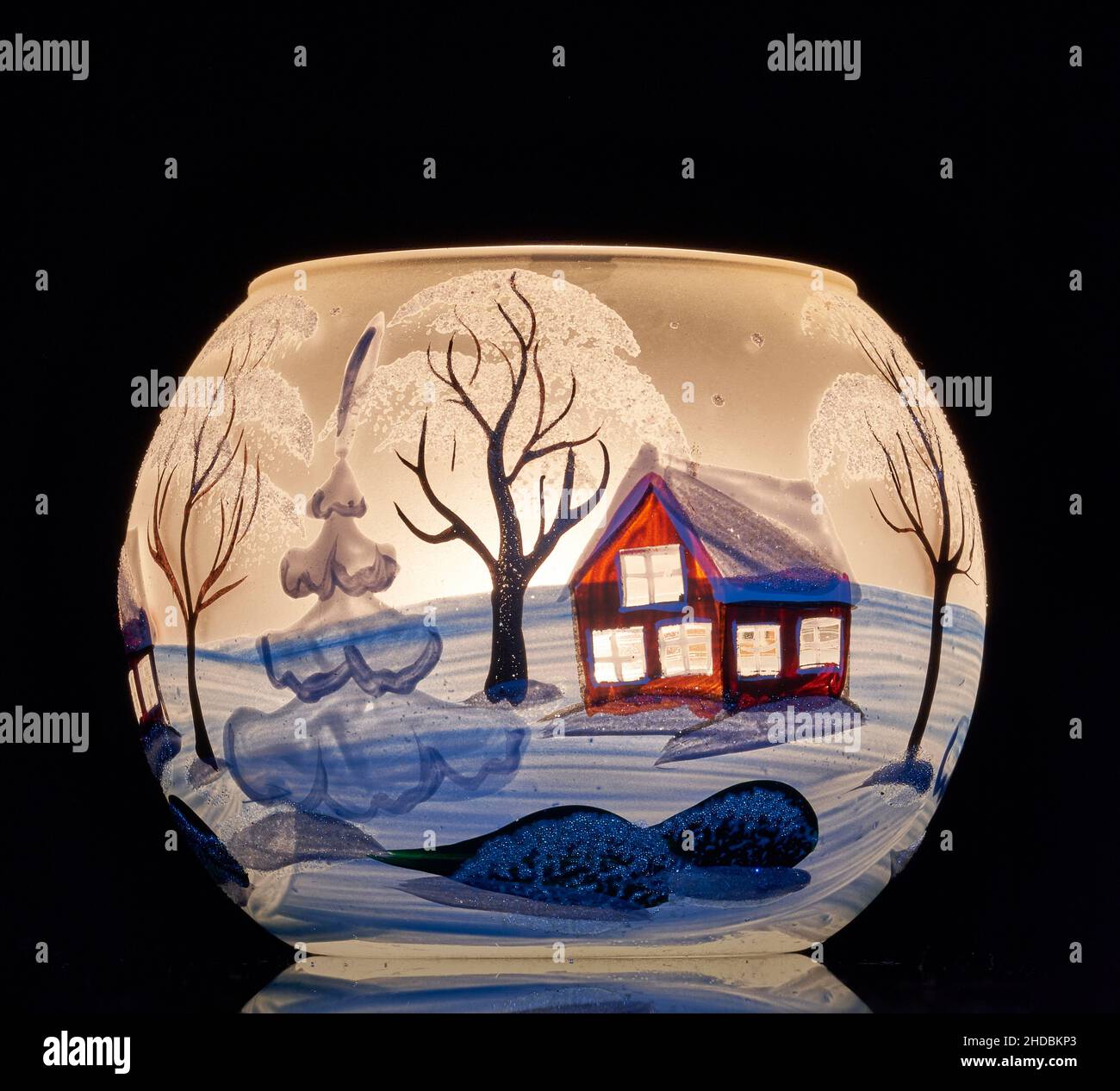 Une tasse en verre peinte à la main avec un décor hivernal éclairé par une bougie à l'intérieur de la tasse.Un gros plan photographique utilisant la peinture légère. Banque D'Images