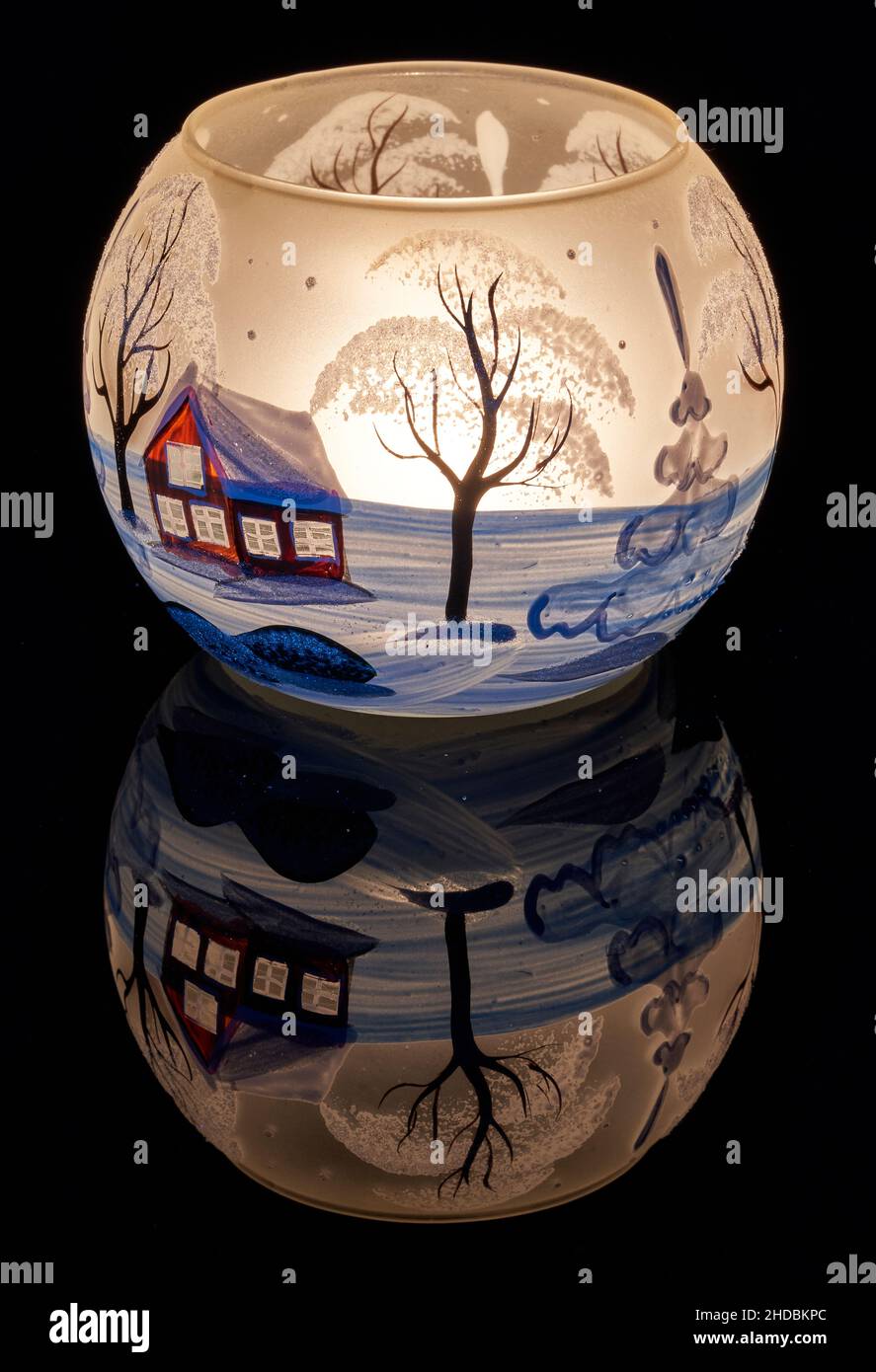 Une tasse en verre peinte à la main avec un décor hivernal éclairé par une bougie à l'intérieur de la tasse.Un gros plan photographique utilisant la peinture légère. Banque D'Images