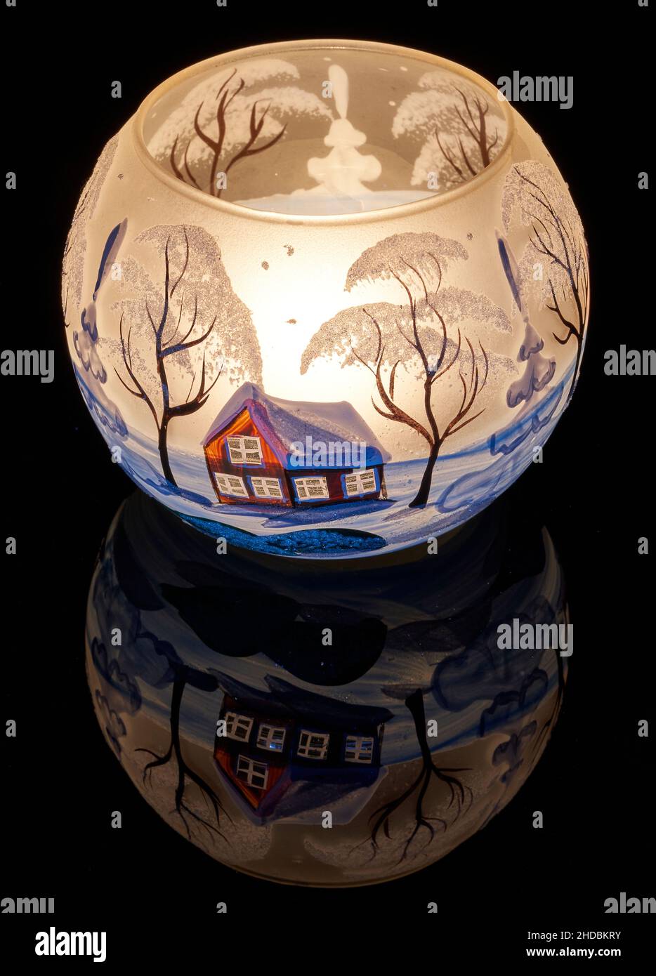Une tasse en verre peinte à la main avec un décor hivernal éclairé par une bougie à l'intérieur de la tasse.Un gros plan photographique utilisant la peinture légère. Banque D'Images