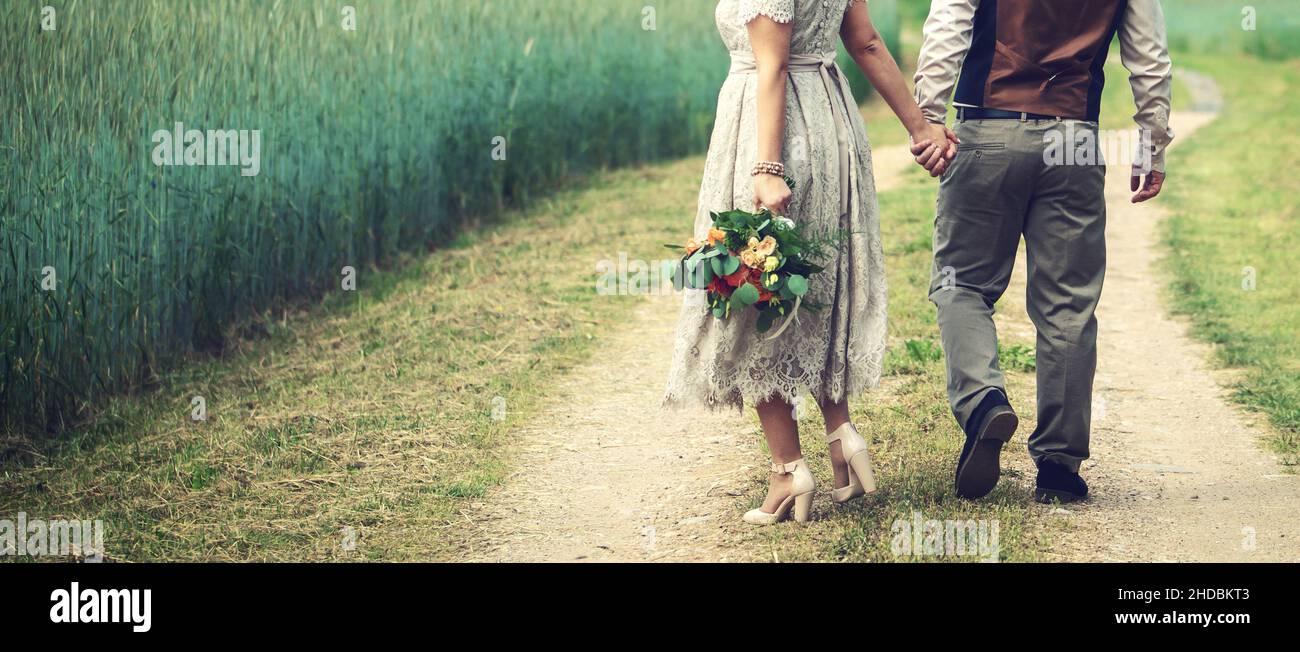 couple de mariage, mariée et marié se tenant les mains et marche la route de campagne à côté du champ de céréales. vue arrière de l'espace de copie Banque D'Images couple de mariage, mariée et marié se tenant les mains et marche la route de campagne à côté du champ de céréales. vue arrière de l'espace de copie Banque D'Images