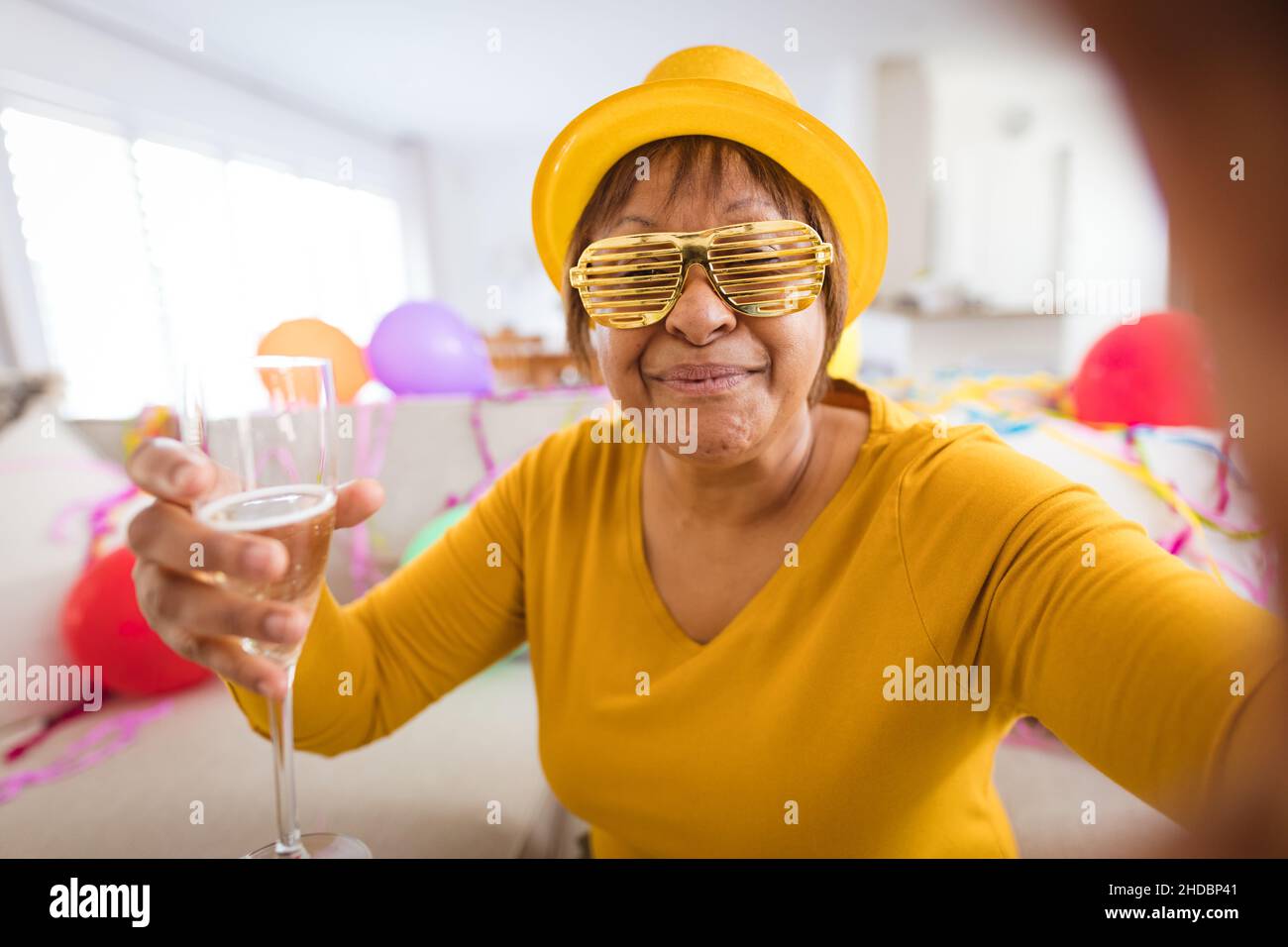 Femme sénior dans des lunettes à obturation pour passer un appel vidéo tout en dégustant du champagne lors d'une fête à la maison Banque D'Images