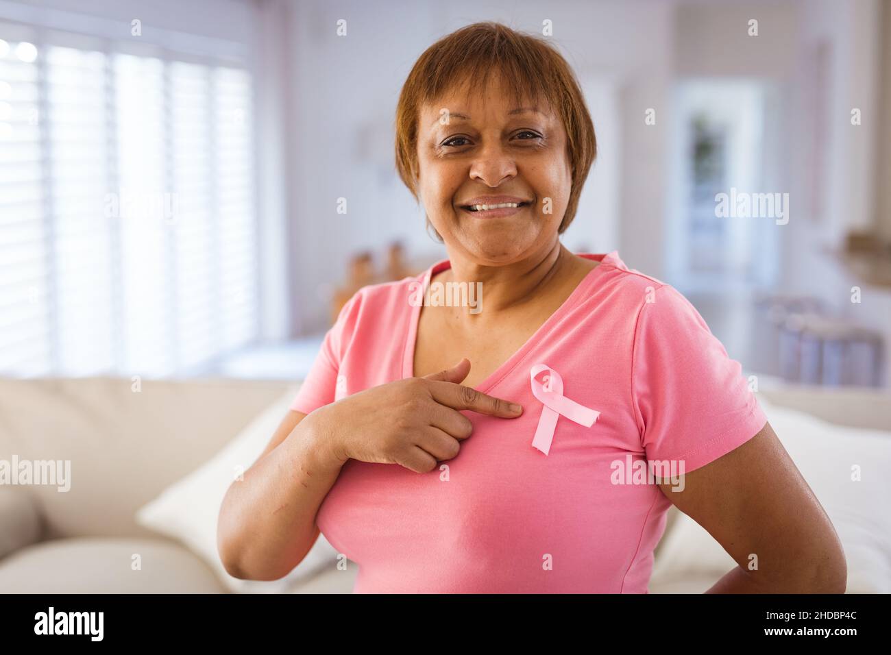 Une femme afro-américaine de haut niveau qui pointe sur un ruban de sensibilisation au cancer du sein sur un t-shirt rose Banque D'Images