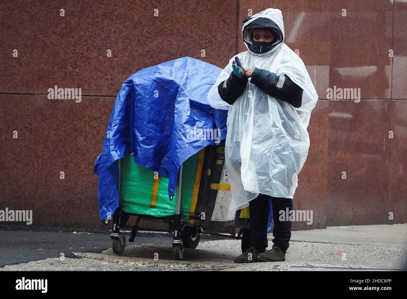 Un préposé à la livraison Amazon attend à un feu de circulation avec des  paquets couverts par une bâche pendant la pluie dans le quartier de  Manhattan à New York, New York,