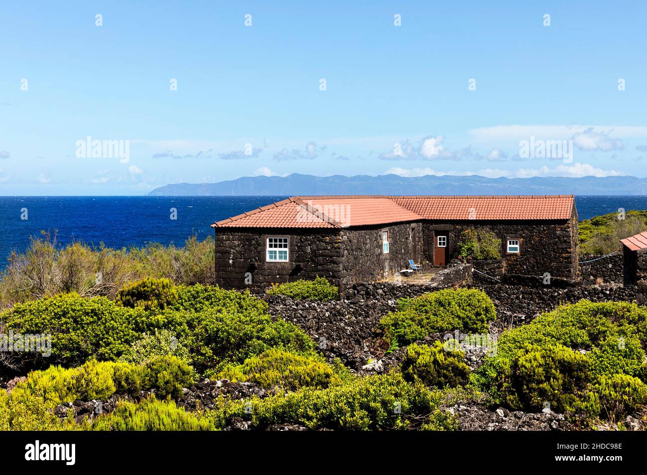 Maison en pierre rurale typique faite de roches volcaniques sur l'île de Pico avec une belle vue sur la mer et l'île de Sao Jorge, Açores, Portugal Banque D'Images
