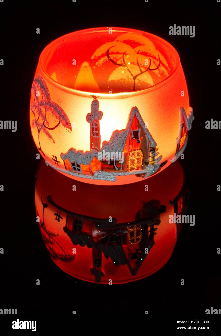 Une tasse en verre peinte à la main avec un décor hivernal éclairé par une bougie à l'intérieur de la tasse.Un gros plan photographique utilisant la peinture légère. Banque D'Images