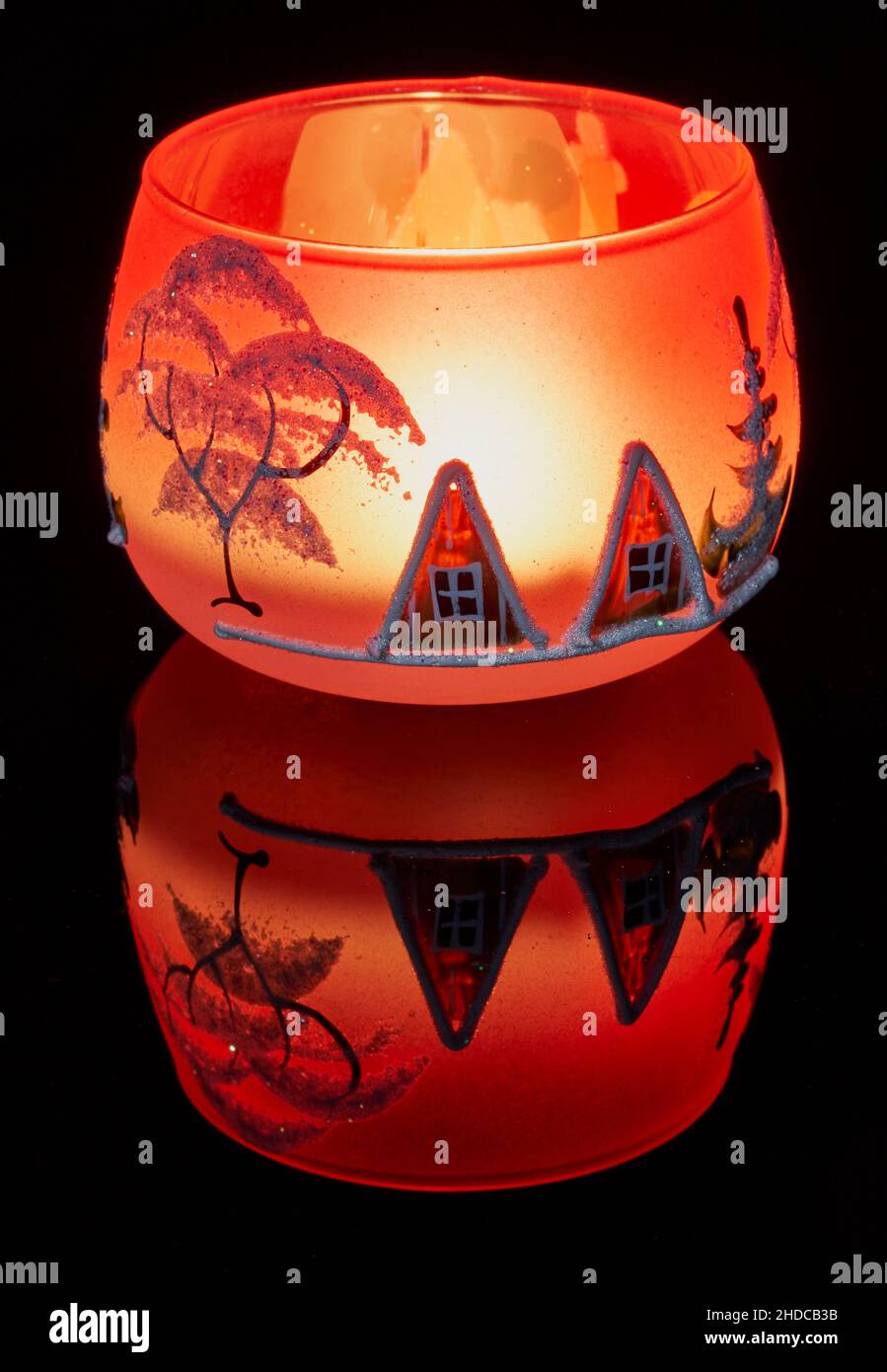 Une tasse en verre peinte à la main avec un décor hivernal éclairé par une bougie à l'intérieur de la tasse.Un gros plan photographique utilisant la peinture légère. Banque D'Images