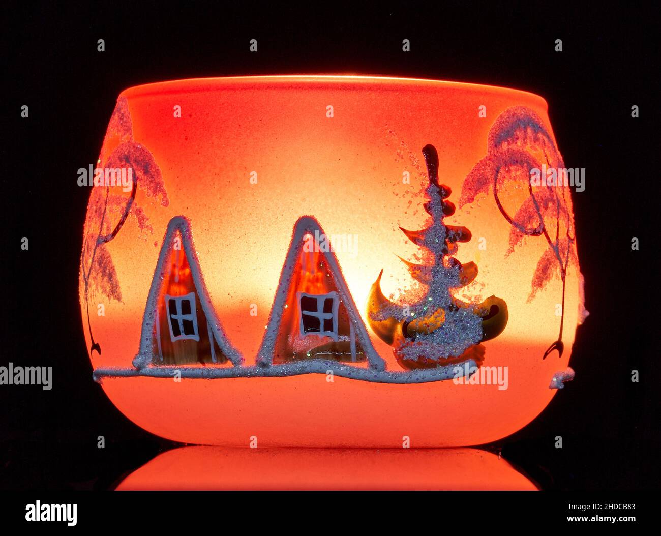 Une tasse en verre peinte à la main avec un décor hivernal éclairé par une bougie à l'intérieur de la tasse.Un gros plan photographique utilisant la peinture légère. Banque D'Images