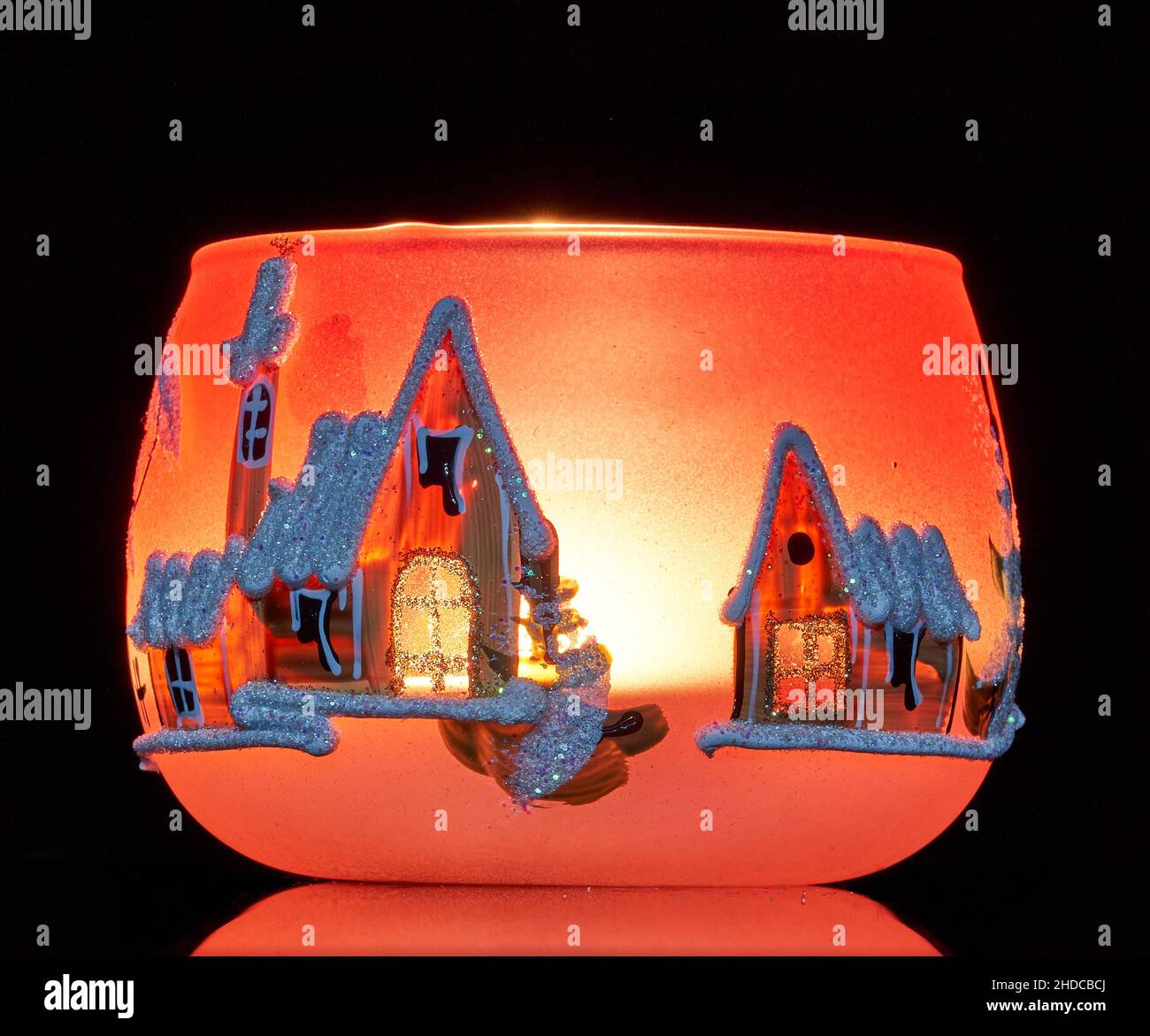 Une tasse en verre peinte à la main avec un décor hivernal éclairé par une bougie à l'intérieur de la tasse.Un gros plan photographique utilisant la peinture légère. Banque D'Images