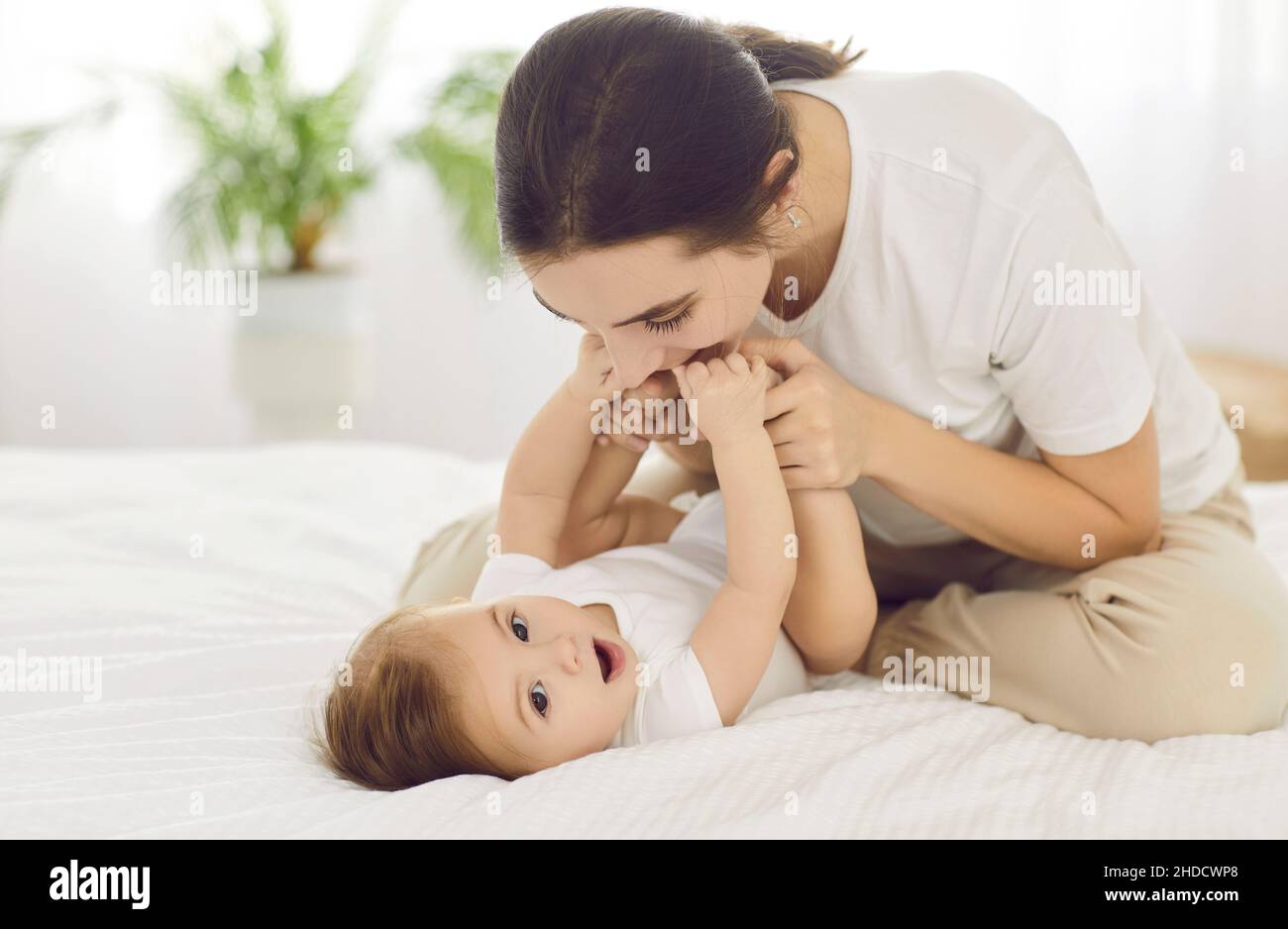 Une jeune mère heureuse et aimante tenant les mains de son bébé garçon et embrassant ses petits pieds Banque D'Images