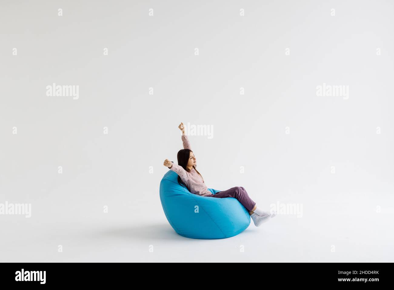 Jeune fille couchée avec les mains levées sur le sac de beanbag isolé sur fond blanc. Banque D'Images