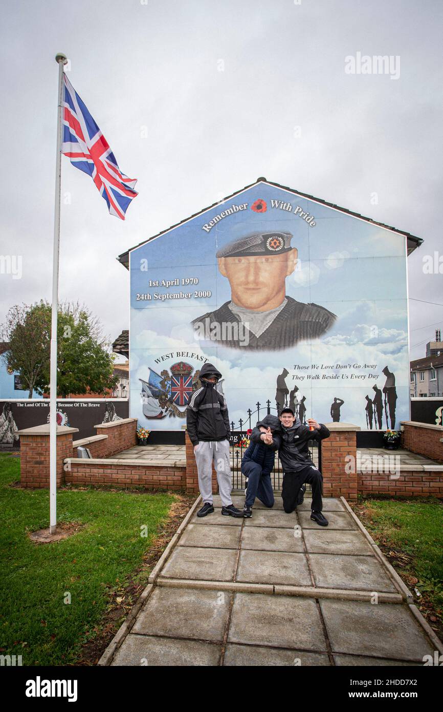 Des jeunes qui posent devant des peintures murales politiques avec des symboles paramilitaires sur le Lower Shankill Estate, à Belfast. Banque D'Images