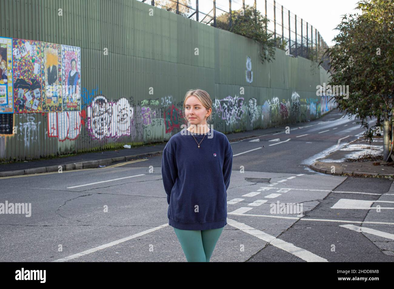 Amy Rafferty, de Trademark, Community Organisation, à l'extérieur de son bureau, avec des peintures murales et graffitis colorés sur le mur de la paix, ou Peace Line, en train de courir le long de la coupe Banque D'Images