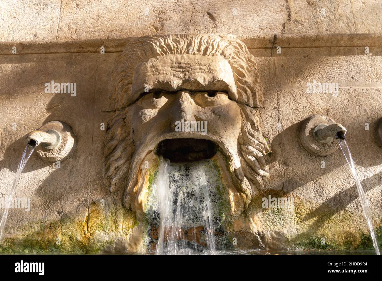 Gros plan d'une fontaine sur le mur avec une statue d'un visage de dieu, eau venant de sa bouche Banque D'Images