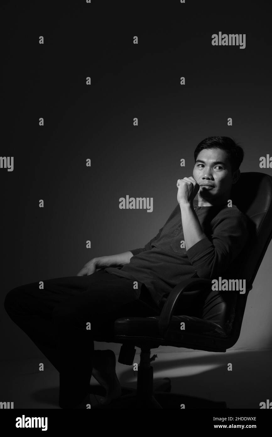 L'homme moderne assis sur une chaise et de style moderne dans le studio, noir et blanc Banque D'Images