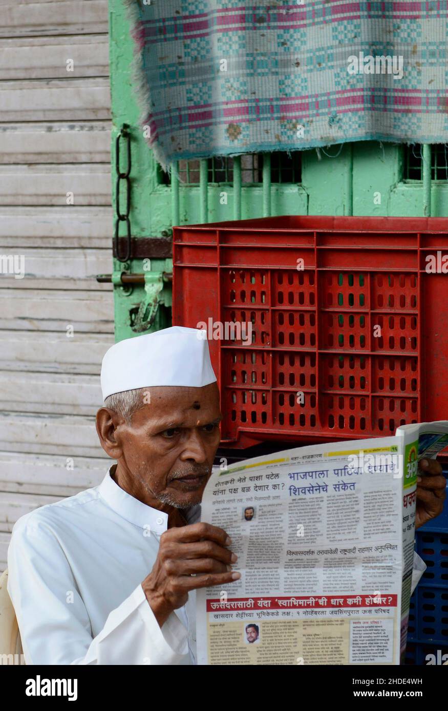 Un homme Mahrati lisant le journal du matin devant un magasin à Mumbai, en Inde. Banque D'Images