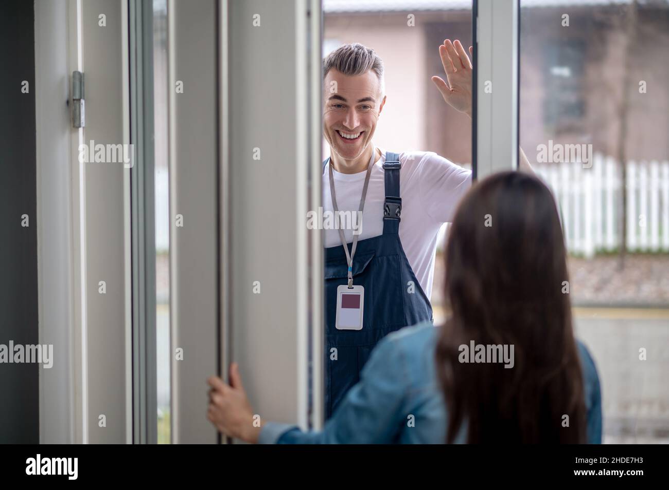 Femme ouvrant la porte à l'homme avec la main levée en salutation Banque D'Images