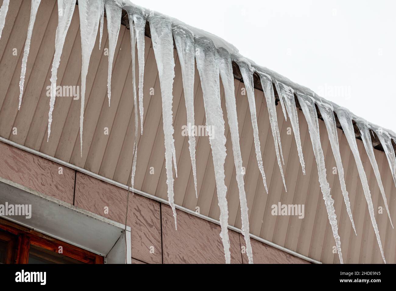 De grandes et longues glaces pendent du toit du bâtiment.Les glaçons constituent un danger pour les piétons. Banque D'Images