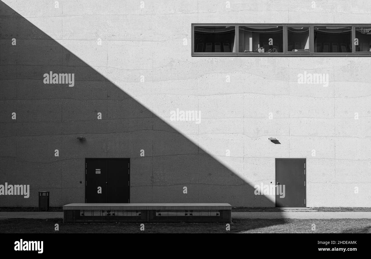 Vue en niveaux de gris d'une porte moderne et de fenêtres dans un mur de pierre moderne clair avec la lumière du soleil Banque D'Images