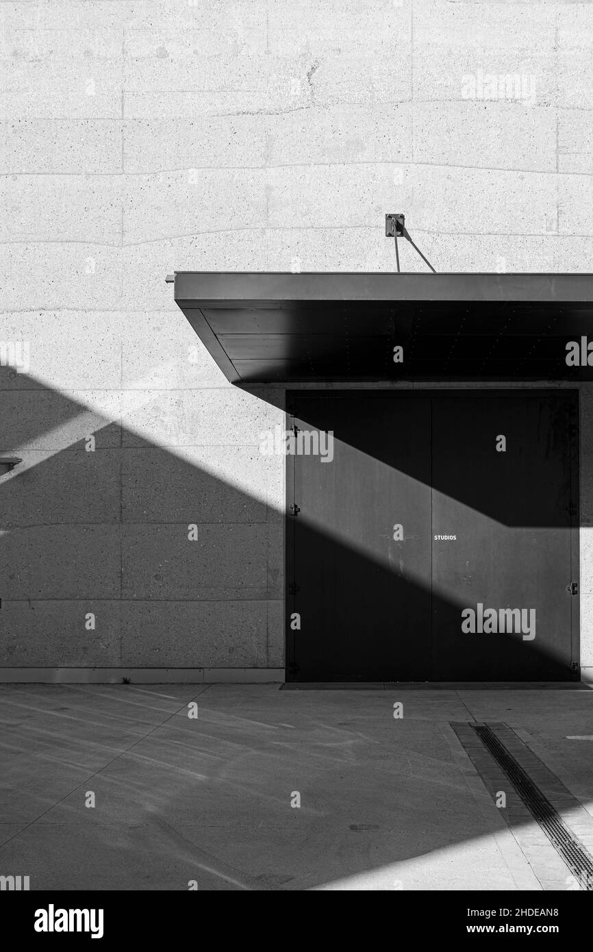 Vue en niveaux de gris d'une porte moderne dans un mur en pierre moderne clair avec lumière du soleil et sol carrelé Banque D'Images