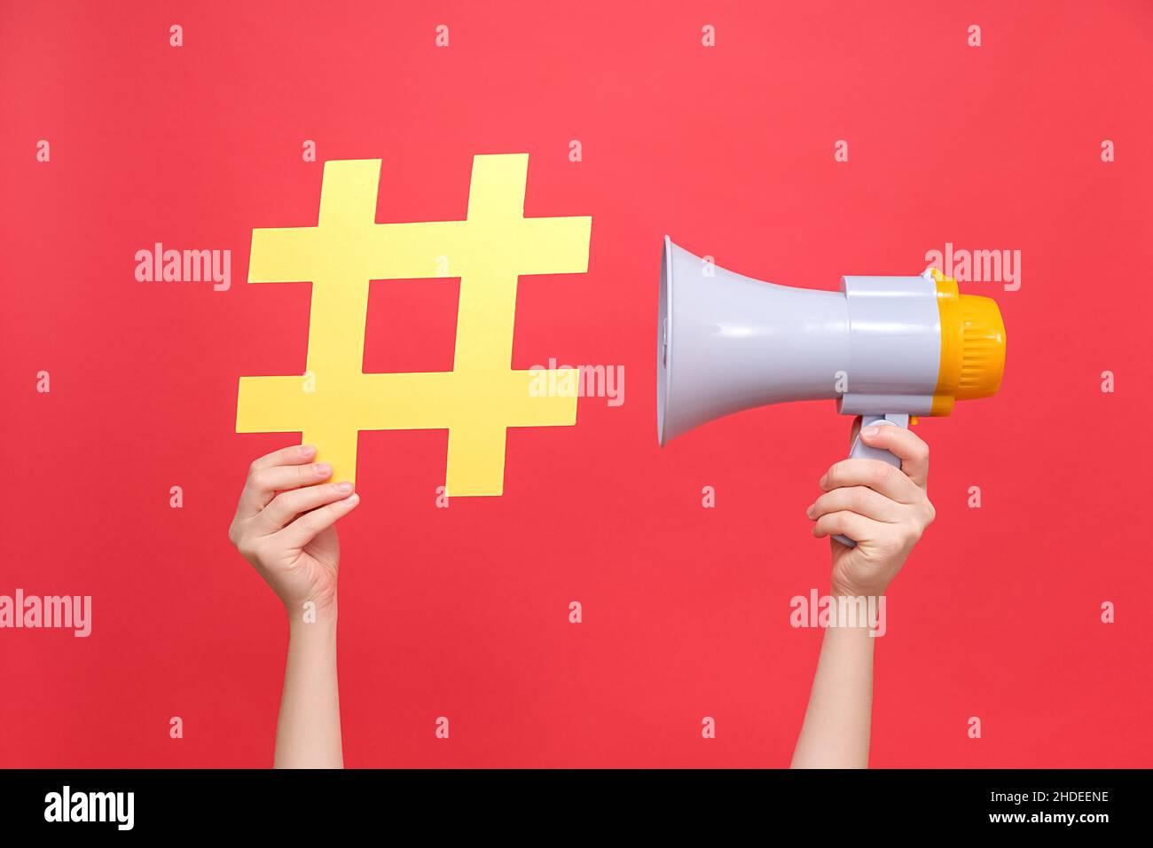 Gros plan des mains de femmes tenant le signe jaune hashtag et le mégaphone, étiquette pour les affaires, le marketing et la publicité, isolé sur fond rouge studio.Con Banque D'Images