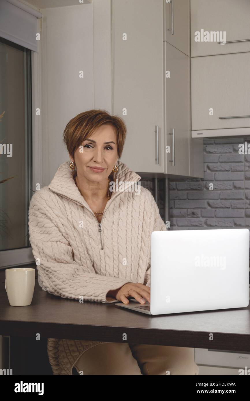 Belle jeune femme d'âge moyen travaillant dans un ordinateur portable.Arrière-plan intérieur gris clair. Banque D'Images