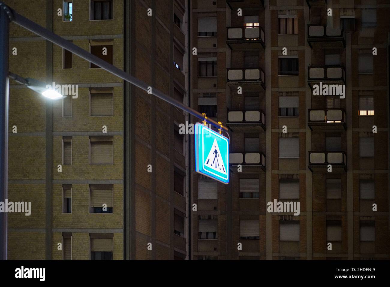 Panneau de signalisation à la lumière vive devant un immeuble résidentiel avec fenêtres éclairées la nuit. Banque D'Images