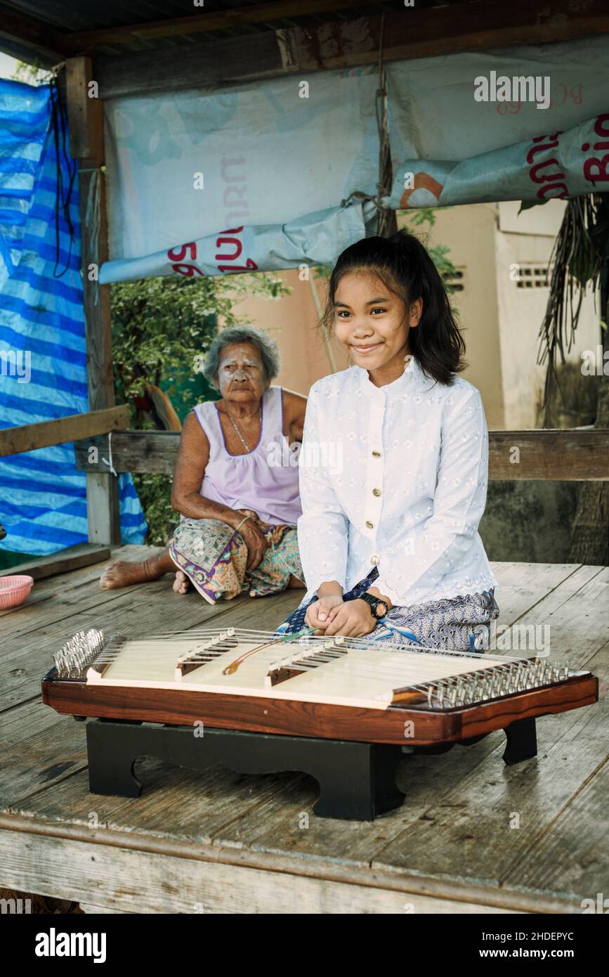 Une belle fille thaïlandaise jouant Khim, la musique thaïlandaise traditionnelle instrument près de la grand-mère à l'extérieur sur panneau de bois.Concept loisir et passe-temps. Banque D'Images