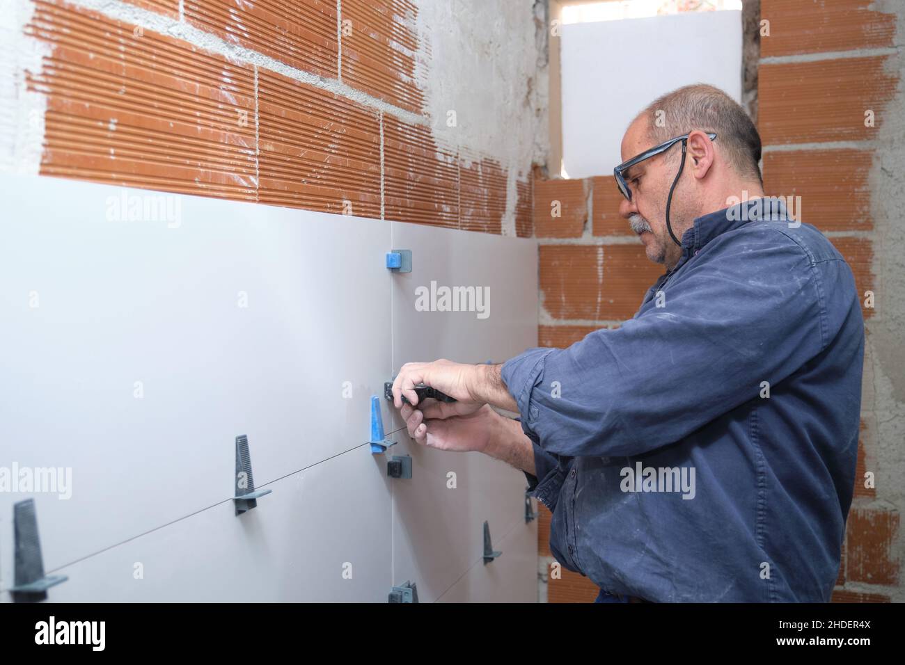 Travailleur senior du constructeur en ajustant la séparation entre les carreaux sur le mur. Banque D'Images