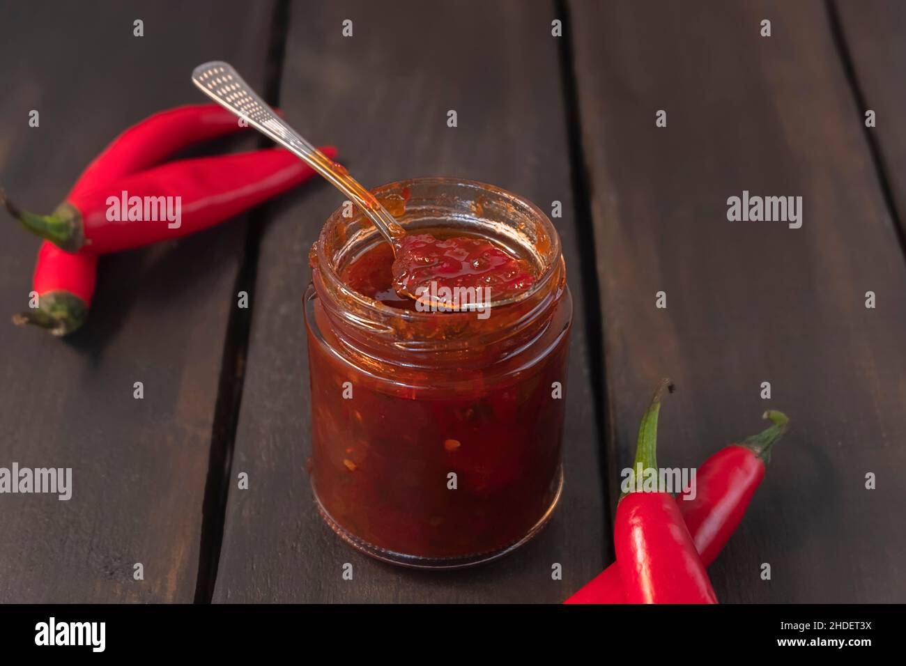 Pot en verre de confiture de piment épicée avec poivrons rouges sur fond de bois Banque D'Images