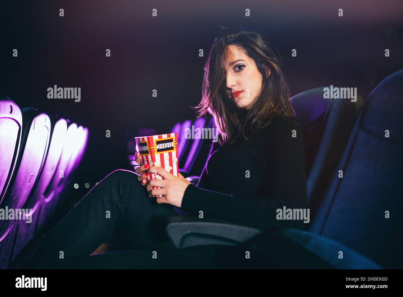 une jeune fille assise au cinéma mange du maïs pop Banque D'Images