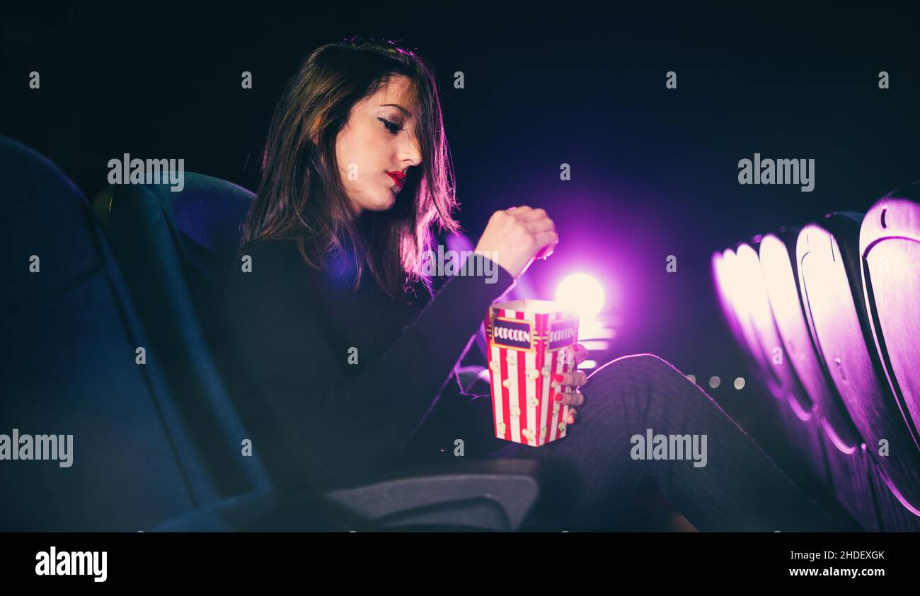 une jeune fille assise au cinéma mange du maïs pop Banque D'Images