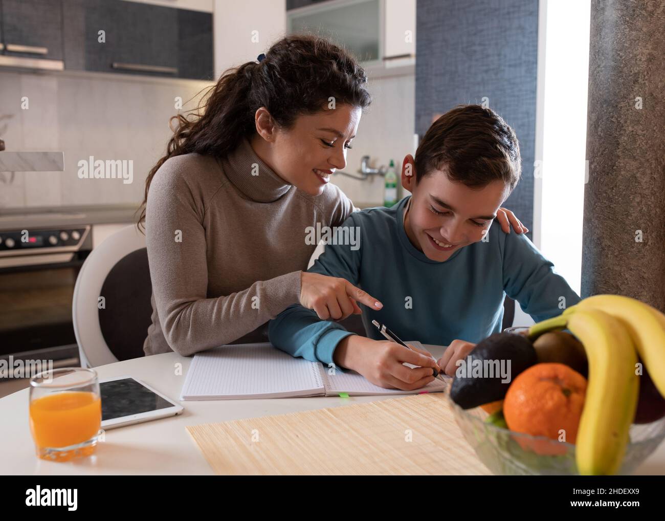 Mère assis avec son fils tout en faisant des devoirs sur table dans la cuisine, souriant, heureux, expression satisfaite Banque D'Images