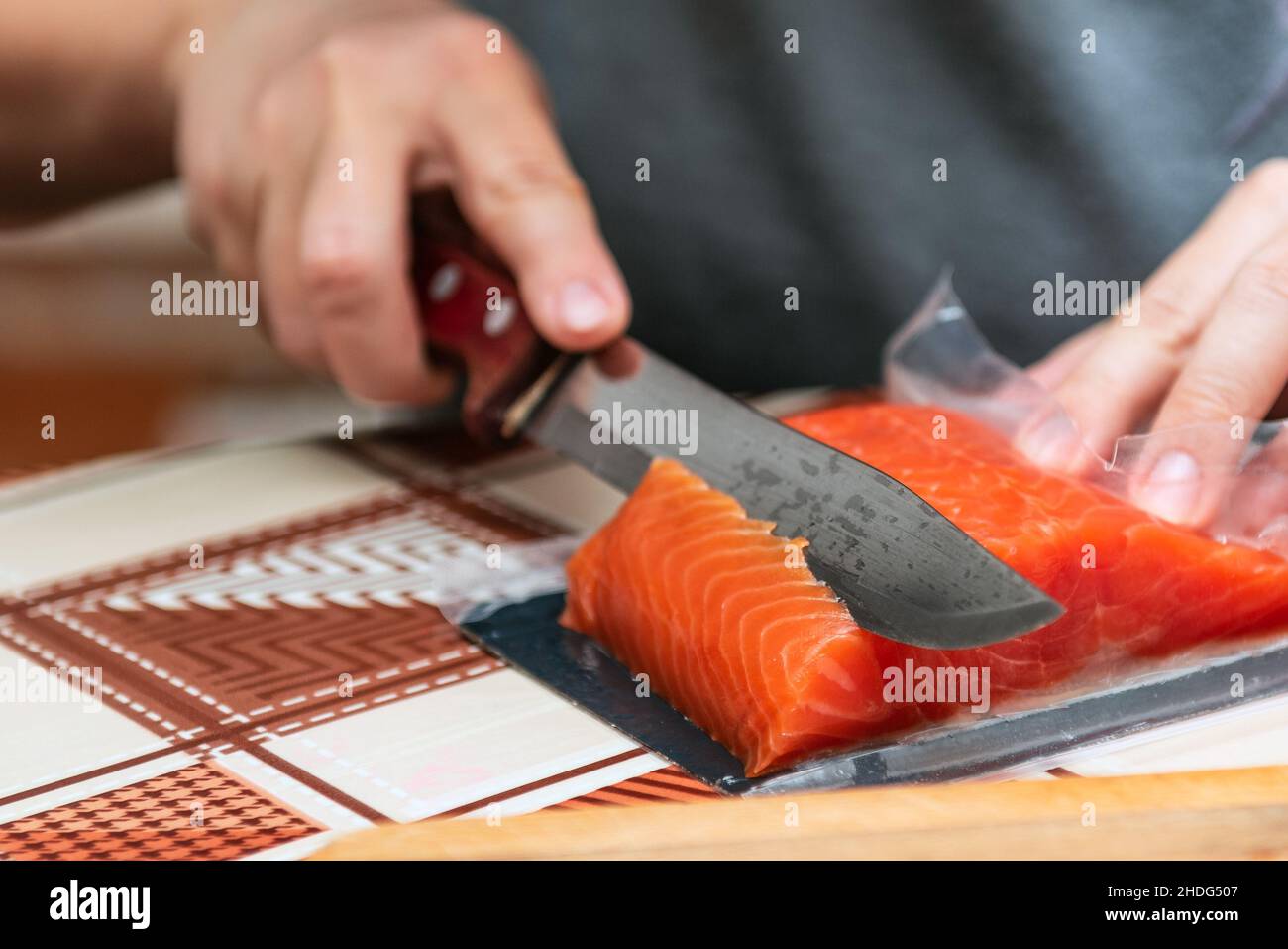 La main avec un couteau coupe le saumon rouge pour les sushis Banque D'Images